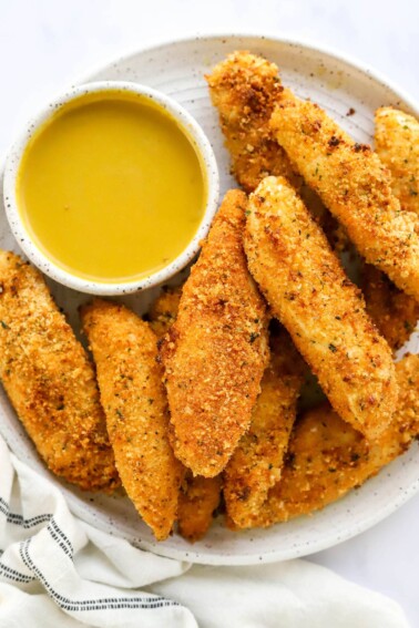 An overhead view of a plate holding air fryer chicken tenders. There is a bowl of honey mustard dipping sauce on the plate with the tenders.