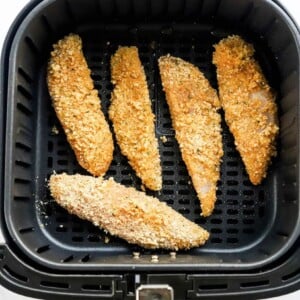 5 dredged chicken tenders spaced at the bottom of an air fryer basket.