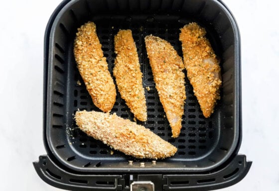 5 dredged chicken tenders spaced at the bottom of an air fryer basket.