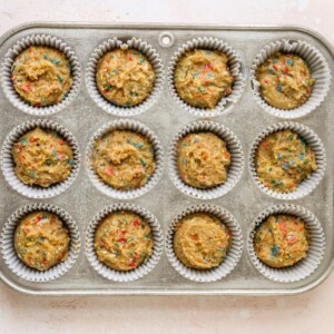 A 12-cavity cupcake tin with paper liners. Cupcake batter has been evenly distributed to all cavities.