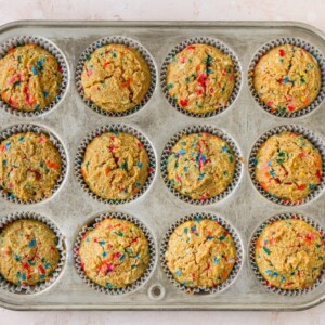 12 baked cupcakes in paper liners in a cupcake tin.