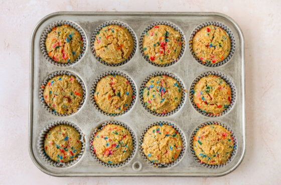 12 baked cupcakes in paper liners in a cupcake tin.