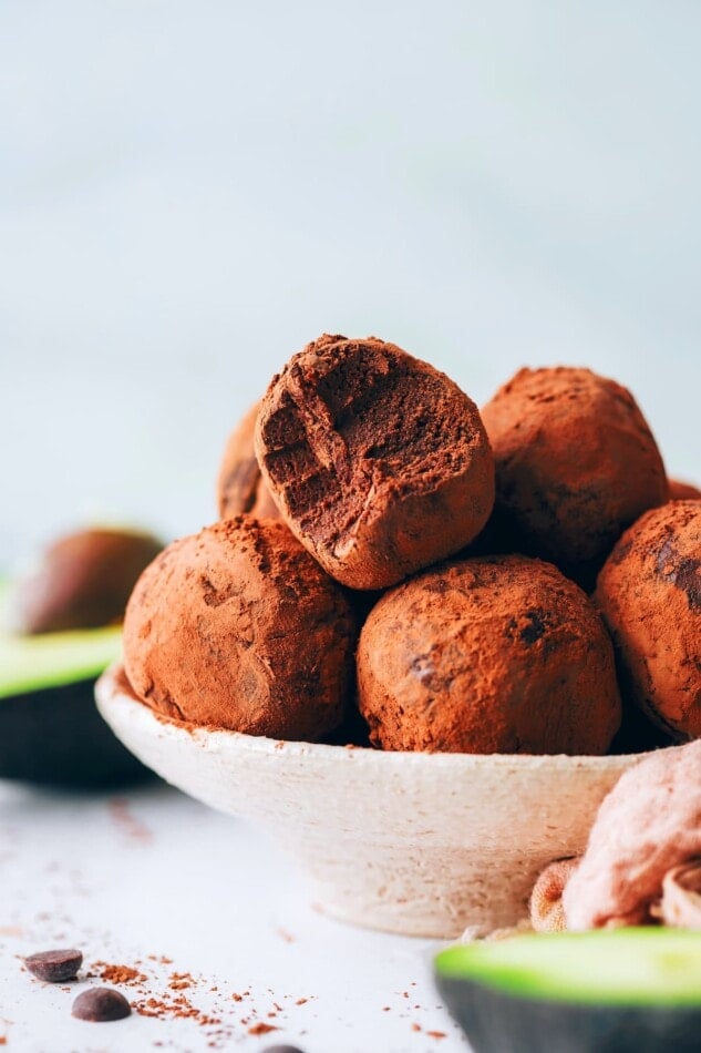A bowl of chocolate avocado truffles. One of the truffles has a bite taken out of it.