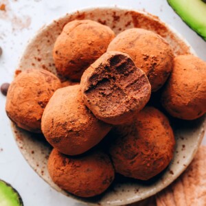 An overhead photo of a bowl of avocado truffles. The top truffle has a bite taken out of it.