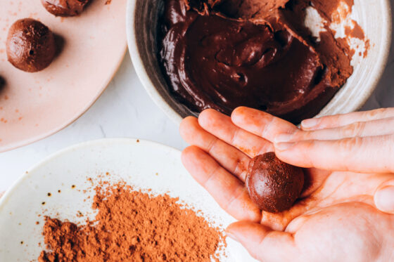 Two hands rolling the chocolate avocado mixture into a ball.