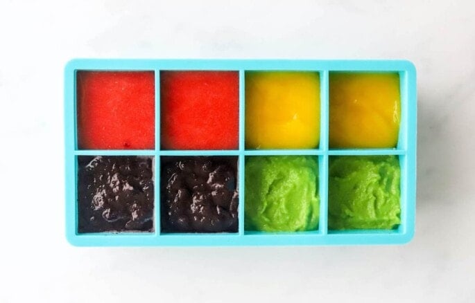 Four different baby food purees in an ice cub tray.