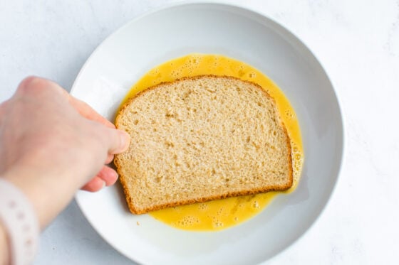 Dipping a slice of bread into the whisked egg.