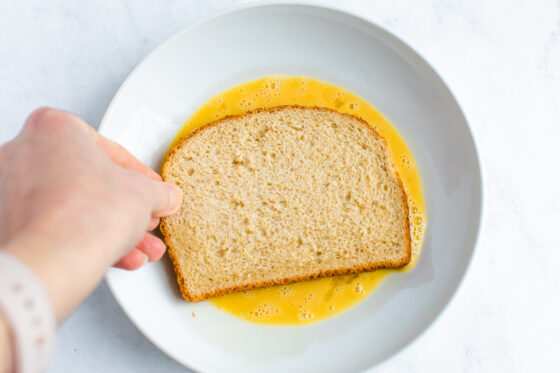 Dipping a slice of bread into the whisked egg.