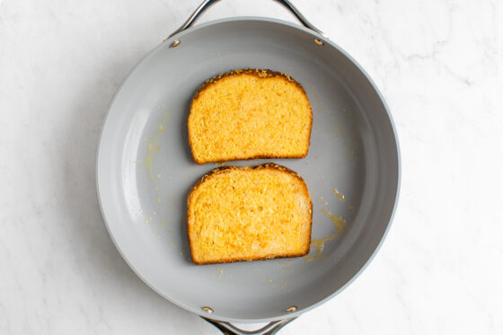 Two slices of bread soaked in egg being cooked on a nonstick pan.