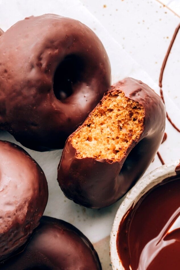 A chocolate covered donut with a bite taken out of it, exposing the inside. There are additional donuts around it.