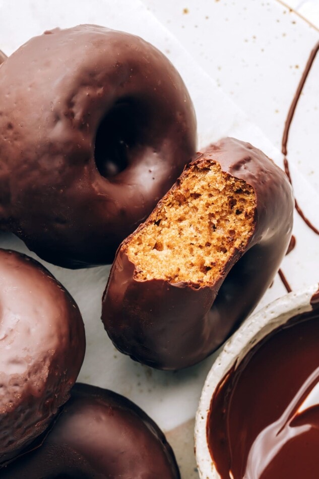 A chocolate covered donut with a bite taken out of it, exposing the inside. There are additional donuts around it.