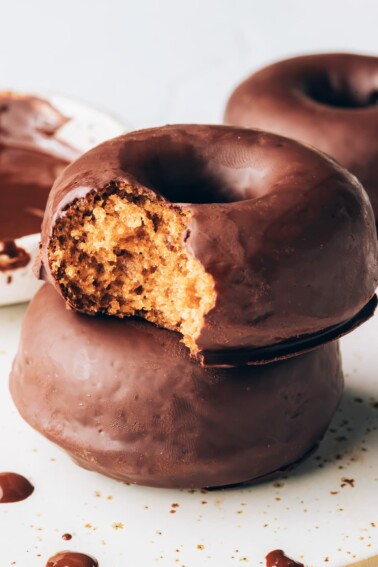 A stack of two donuts. The top donut has a bite taken out of it.