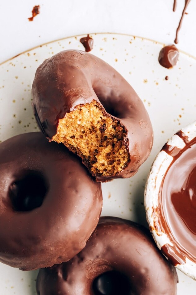 Three donuts on a plate. The first donut has a bite taken out of it.