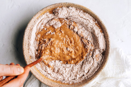 A wooden spoon held by a hand is mixing together the wet and dry ingredients.