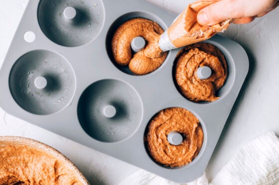 A hand using a pastry bag to pipe donut batter into the donut pan cavities.