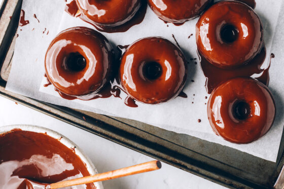 Freshly coated chocolate donuts on a sheet pan lined with parchment paper.