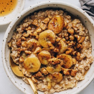 An overhead photo of a bowl of banana bread oatmeal, topped with banana slices and walnuts, and drizzled with maple syrup.
