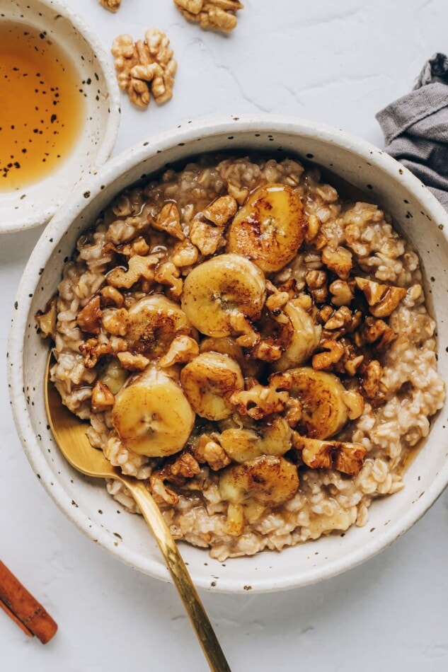 An overhead photo of a bowl of banana bread oatmeal, topped with banana slices and walnuts, and drizzled with maple syrup.