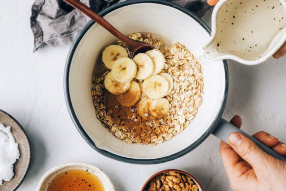 A sauce pot with oats, cinnamon, vanilla, sea salt and banana slices. Water is being poured in.