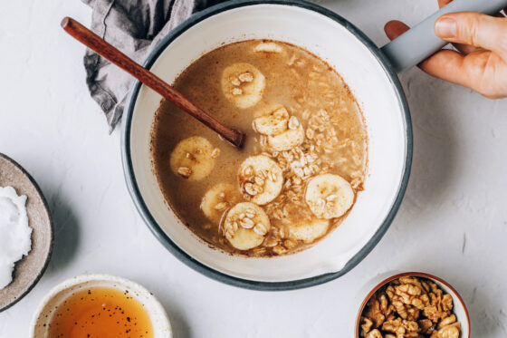 A sauce pot with water, oats, cinnamon, vanilla, sea salt and banana slices mixed together.