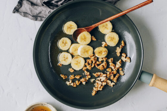 Banana slices and walnuts added to a sauté pan with maple syrup and coconut oil.