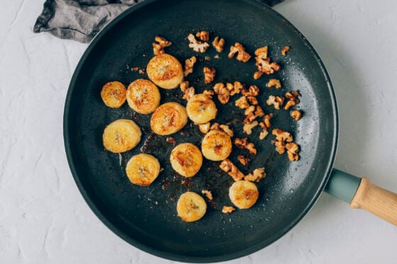 Caramelized banana slices and walnuts in a sauté pan.