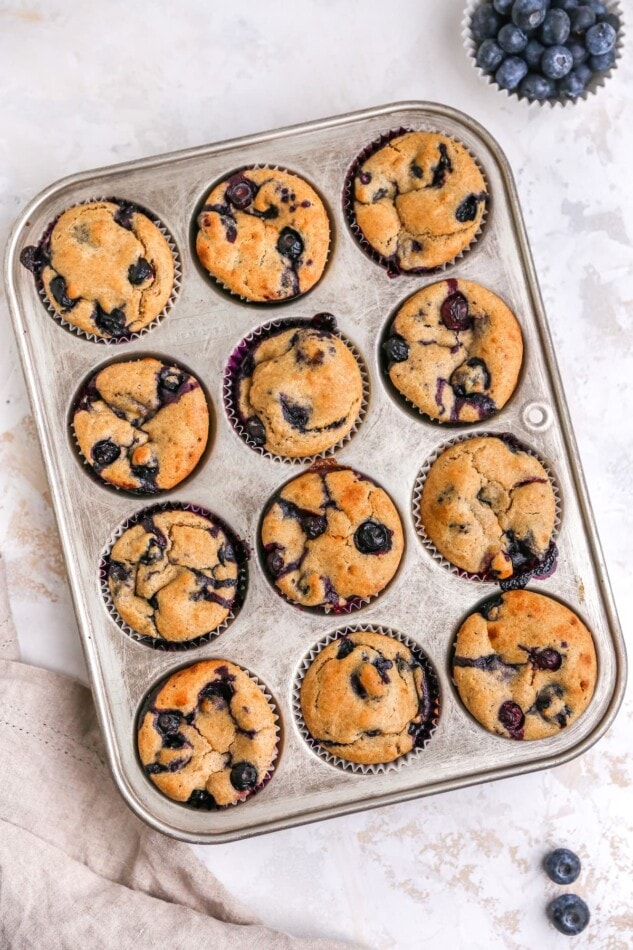 A 12 muffin tin containing freshly baked greek yogurt muffins with blueberries.