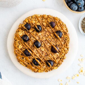 An overhead photo of a small plate with an oatmeal breakfast cookie on top. A small container of blueberries and chia seeds are next to the plate as well as a mug of tea.