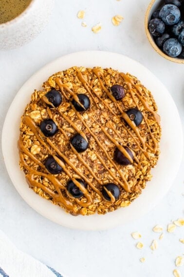 An overhead photo of a small plate with an oatmeal breakfast cookie on top. A small container of blueberries and chia seeds are next to the plate as well as a mug of tea.