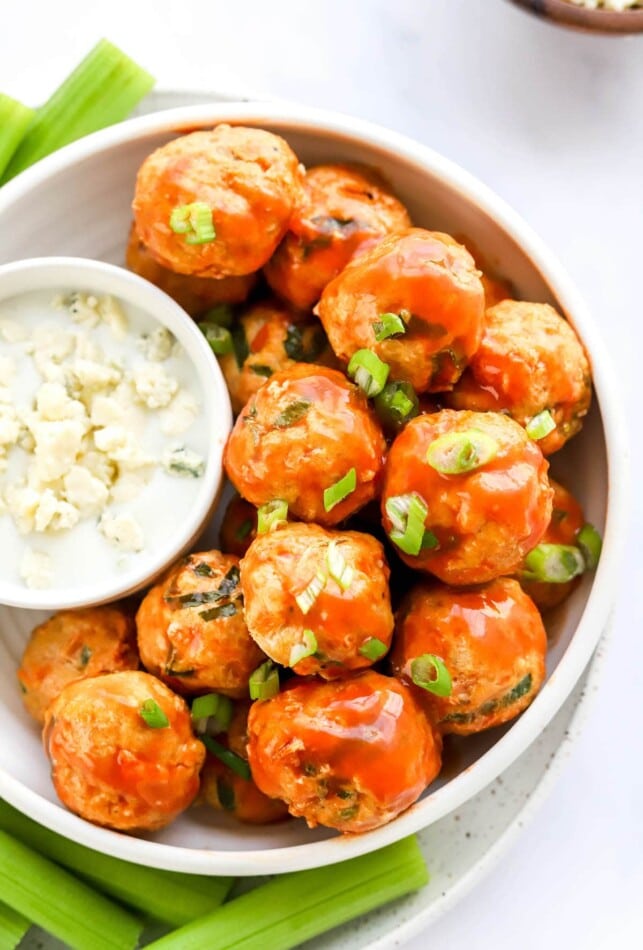 A bowl of buffalo chicken meatballs. A small dish with blue cheese rests in the bowl with the meatballs.
