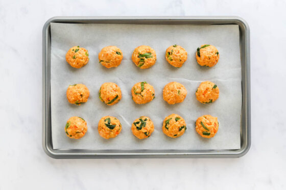 Fifteen uniform meatballs on a parchment lined baking sheet.