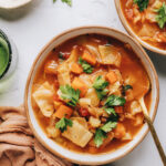 A birds eye view of a bowl of cabbage soup, there is a second bowl cut out of frame.