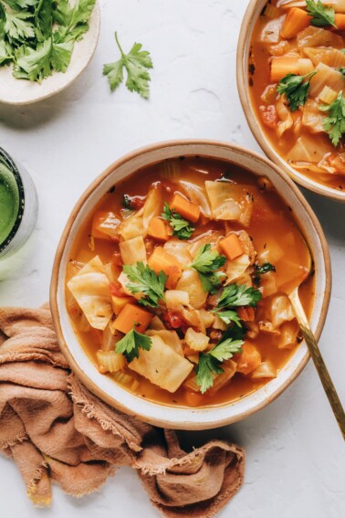 A birds eye view of a bowl of cabbage soup, there is a second bowl cut out of frame.
