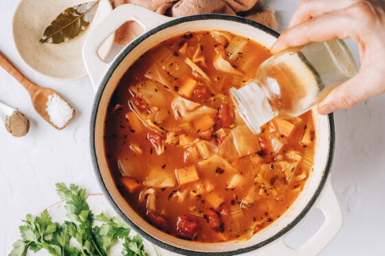 Pouring in remaining apple cider vinegar to the pot of cabbage soup. The bay leaf has been removed.