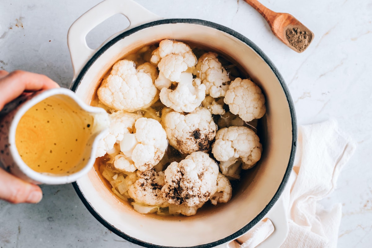 Salt, pepper, cauliflower and vegetable broth being added to the stock pot.