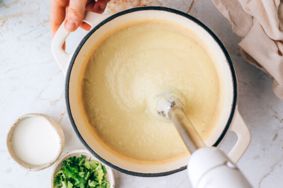 An immersion blender blending up cauliflower soup in a stock pot.