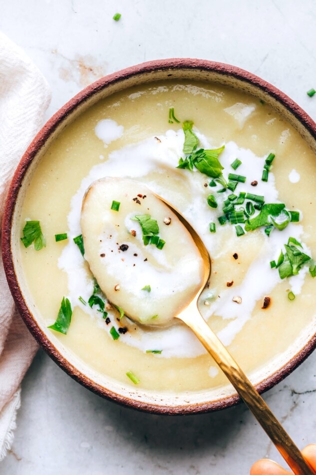 A bowl of cauliflower soup. A spoon is lifting a spoonful out of the bowl.