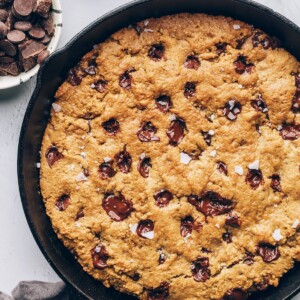 A cast iron skillet containing a baked chocolate chip cookie that encompasses the entire skillet.