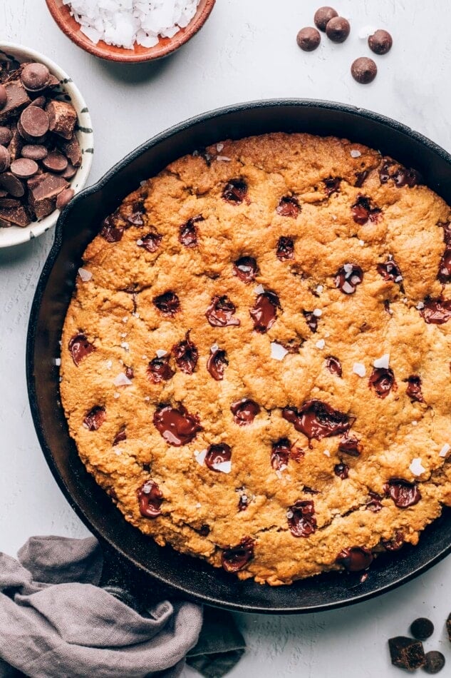 A cast iron skillet containing a baked chocolate chip cookie that encompasses the entire skillet.