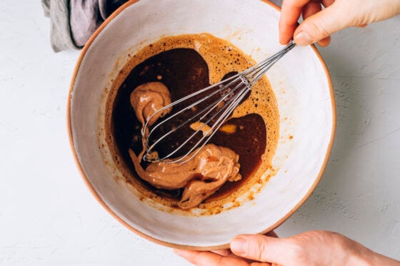 Coconut oil, almond butter, vanilla extract added to the egg and sugar mixture. The ingredients are being whisked together.