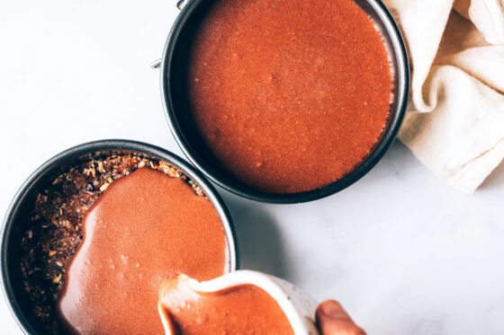 Two mini spring form pans with the coconut, pecan and date mixture. The chocolate mixture is being poured overtop of the crust.