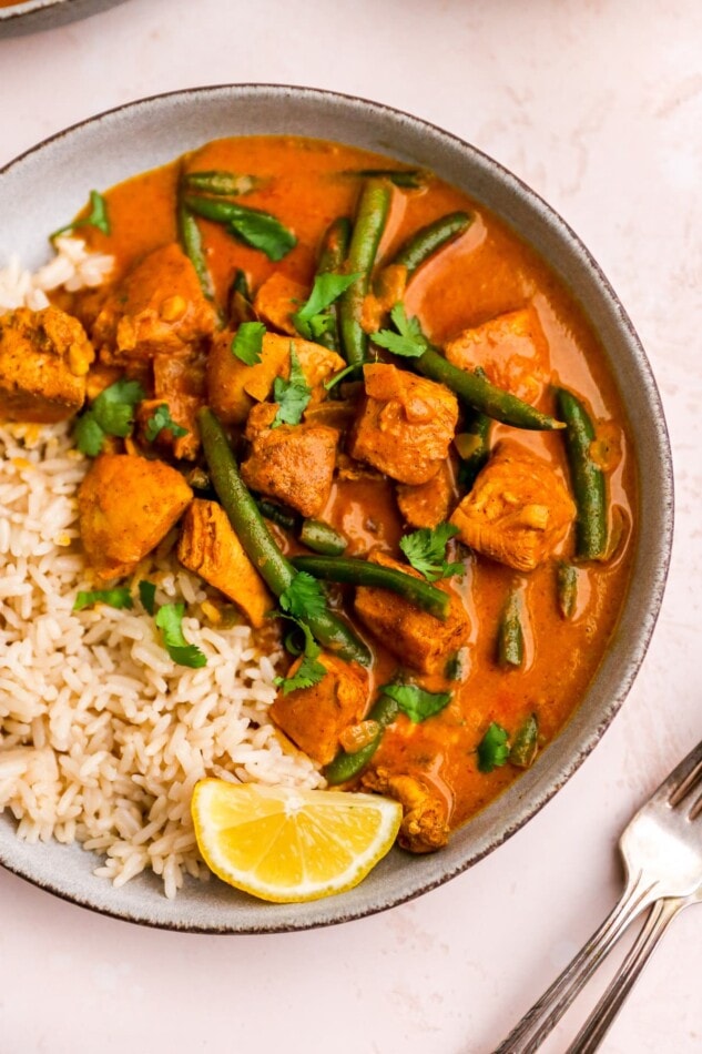 A birds eye view of a bowl of butter chicken. Half the bowl has rice.