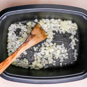 Garlic and onion sautéing in oil in the bottom of a slow cooker.
