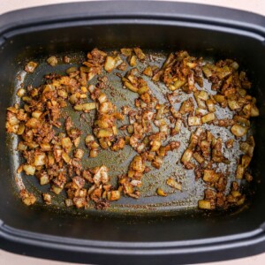 Spices mixed together with onions and garlic in a slow cooker.