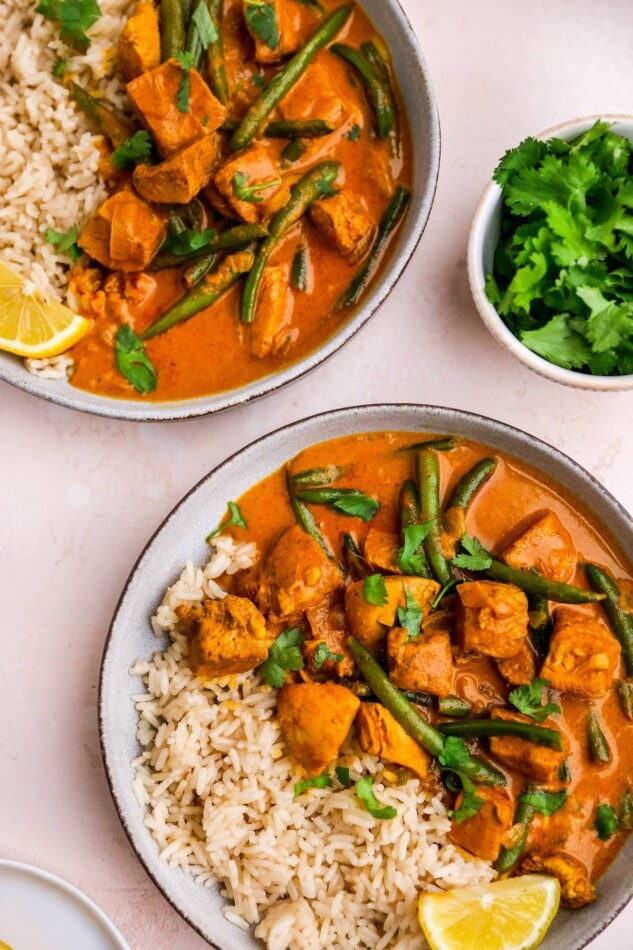 A birds eye view of two bowls of butter chicken. Each bowl has half rice, half butter chicken.