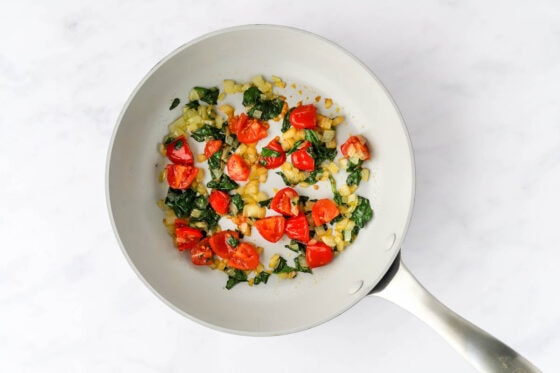 Tomatoes, spinach, onion, salt and pepper sautéing in a pan.