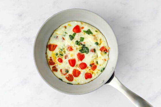 Egg whites poured into the sautéed vegetables in a pan.