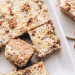 Overhead photo of a baking dish with oatmeal cake. Half of the cake has been sliced into squares with a few removed.