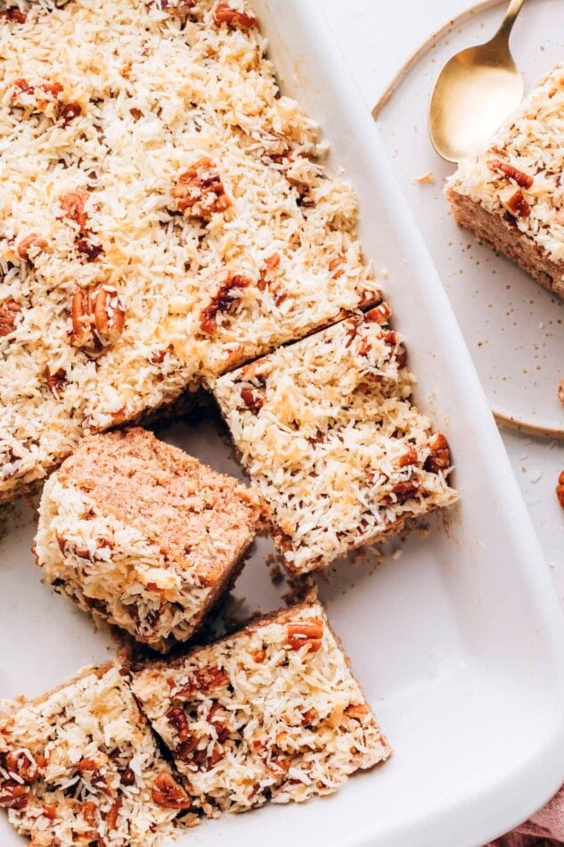 Overhead photo of a baking dish with oatmeal cake. Half of the cake has been sliced into squares with a few removed.