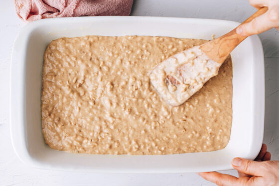 Cake batter poured into the prepared 9x13 baking dish. A wooden spoon is leveling the mixture.